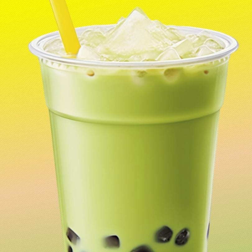 Green boba tea with ice and a yellow straw in a clear plastic cup.