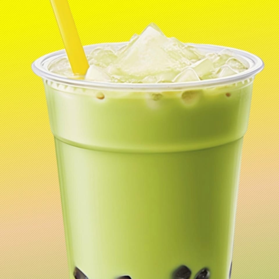 Green boba tea with ice and a yellow straw in a clear plastic cup against a yellow background.