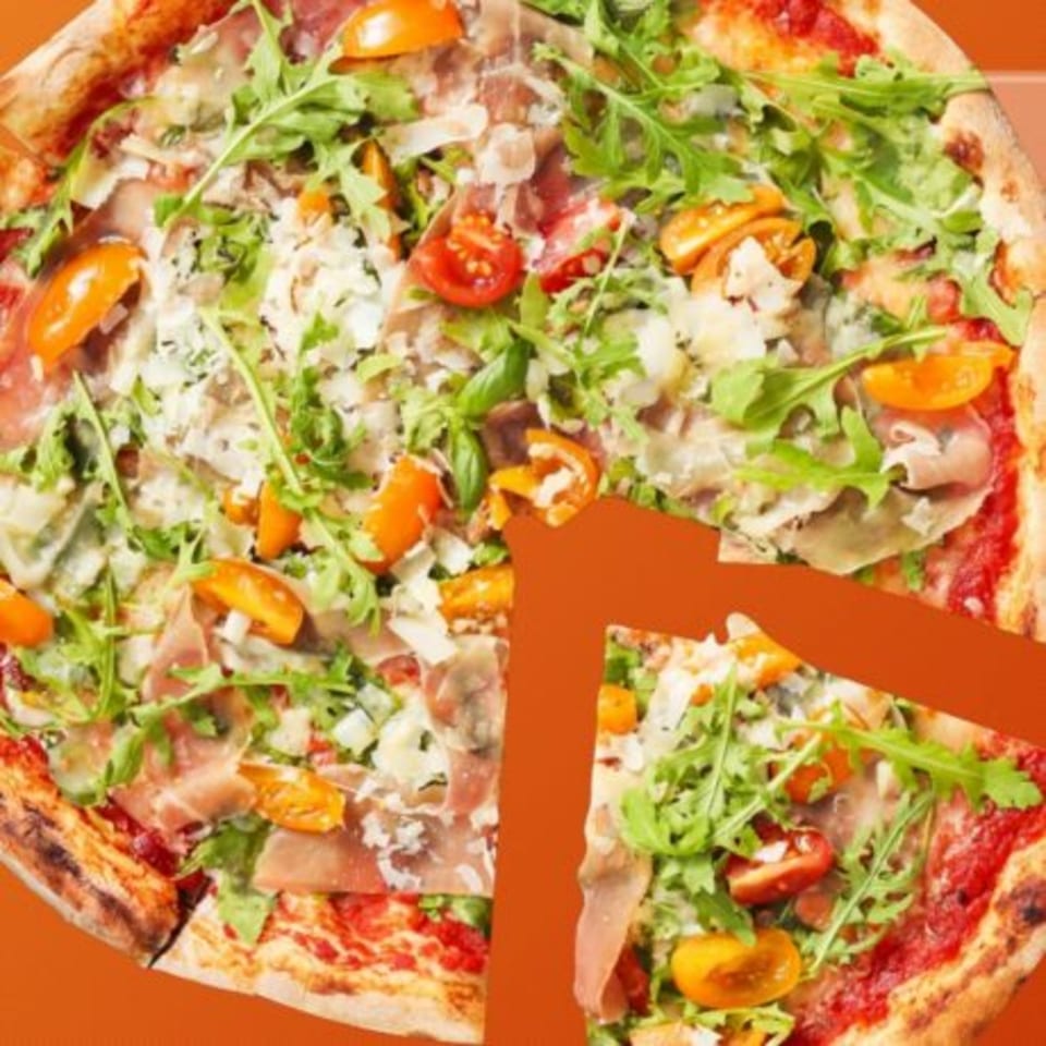 A whole pizza with prosciutto, arugula, cherry tomatoes, and parmesan cheese, with one slice removed.